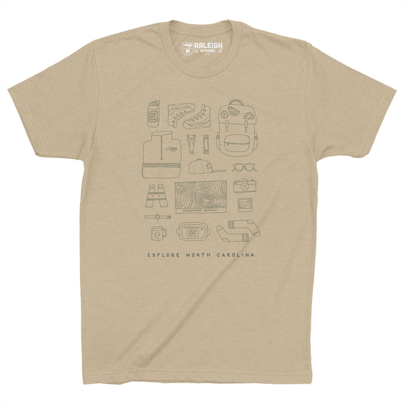 Cream colored t-shirt with different hiking accessories such as boots, backpack, topo map, binoculars, sunglasses and more, drawn in black print. Bottom of the shirt says Explore North Carolina.