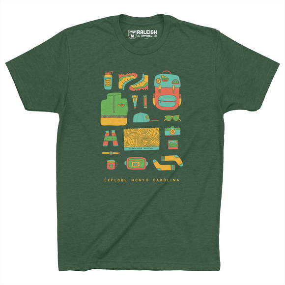 Forest green t-shirt with different hiking accessories such as boots, backpack, topo map, binoculars, sunglasses and more, in bright colors. Bottom of the shirt says Explore North Carolina in yellow.