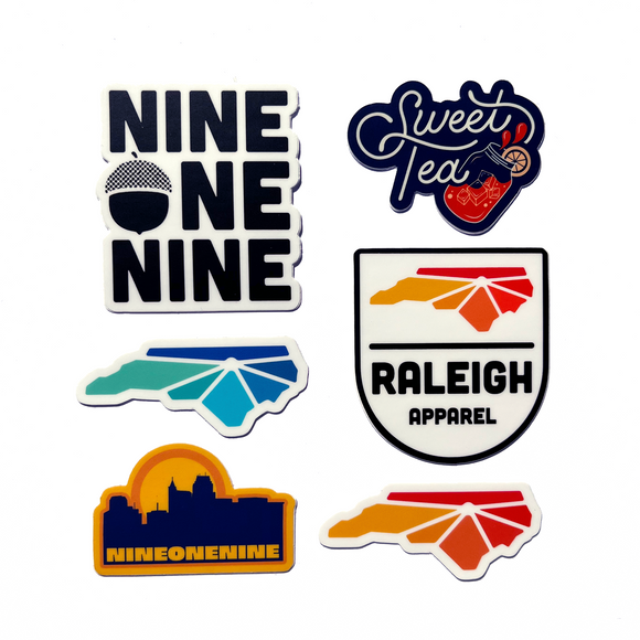 6 stickers in pack. Sweet Tea in Navy with mason jar glass of tea. Nine One Nine with acorn replacing O. Raleigh Apparel logo in cool colors. Raleigh Apparel logo in warm colors. Raleigh skyline in navy with yellow background. Raleigh Apparel badge with warm colors
